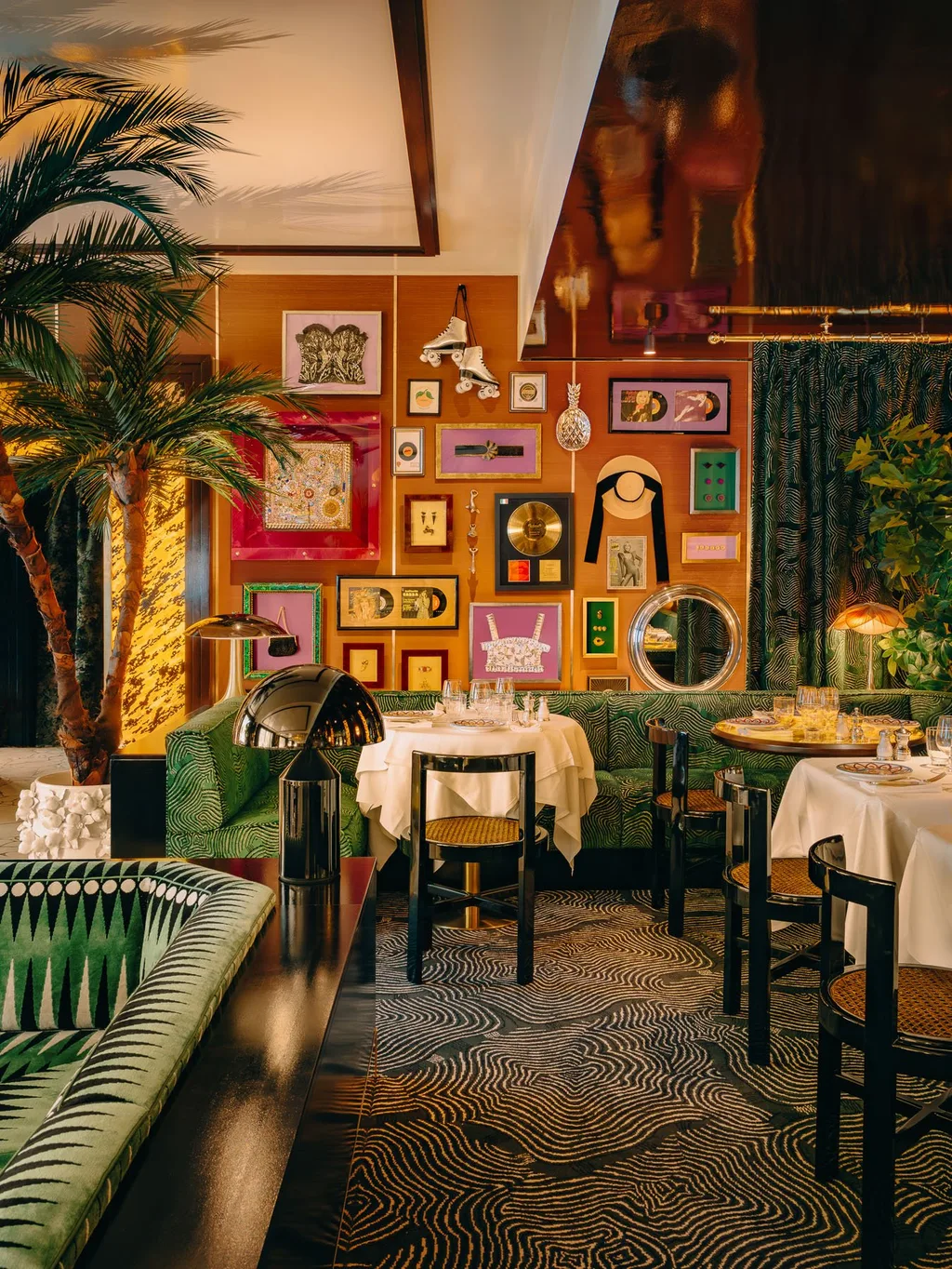 Palm tree and green patterned seating beside a wall of framed artworks at Big Mamma, UK
