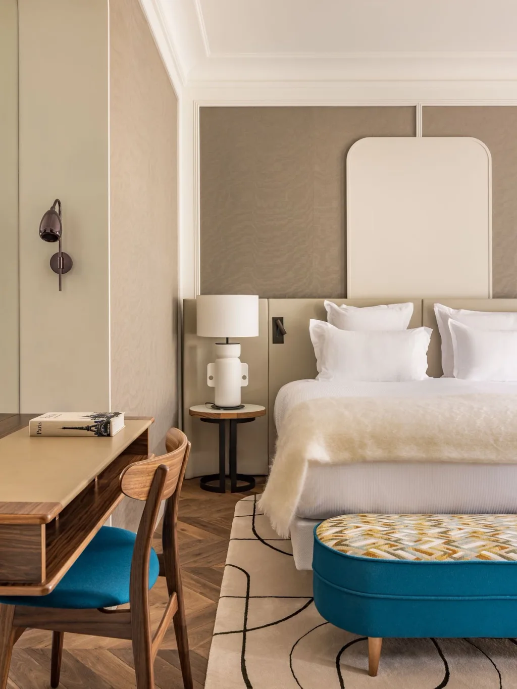 Bedroom with taupe upholstered wall panels and a patterned blue bench at Hotel Pavillon St Germain, Paris
