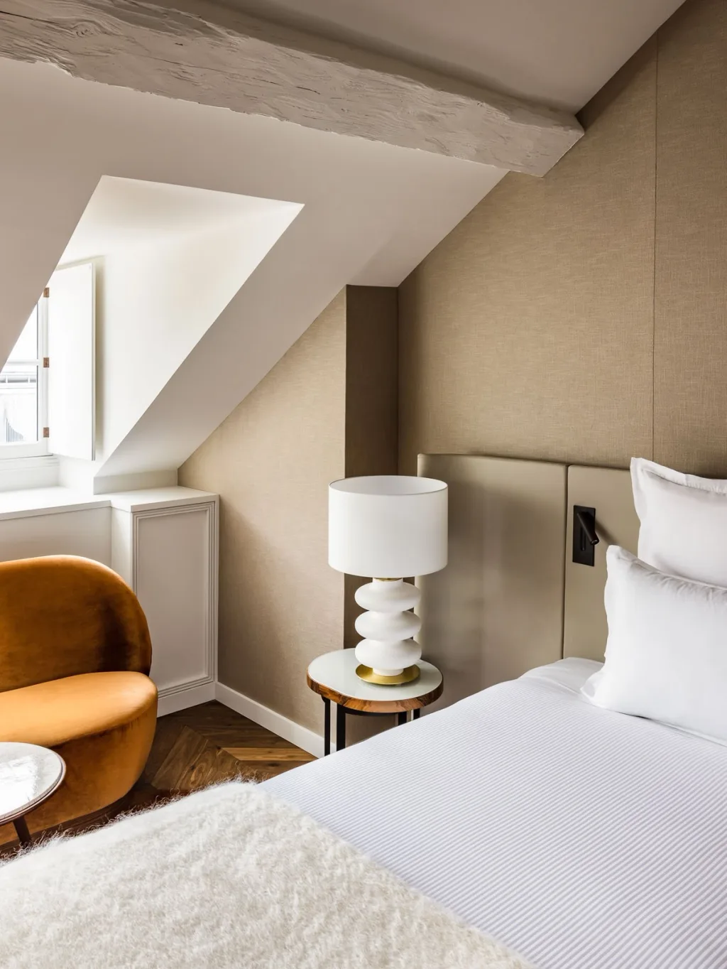 Attic bedroom with sloped beams and a burnt-orange velvet armchair at Hotel Pavillon St Germain, Paris