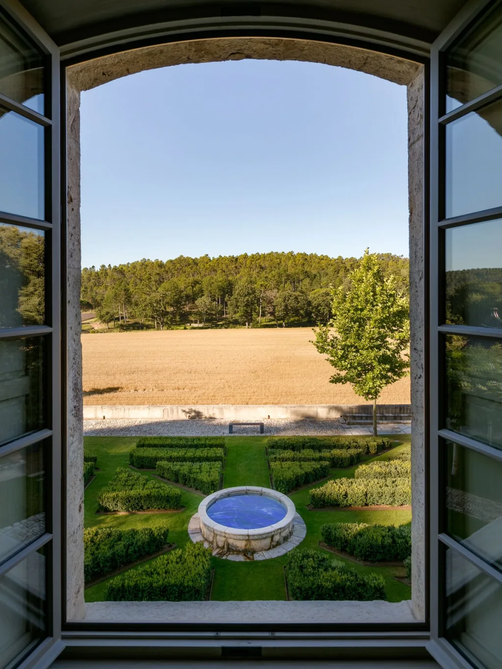 Open window overlooking clipped hedges and a round garden fountain at Fabrègues