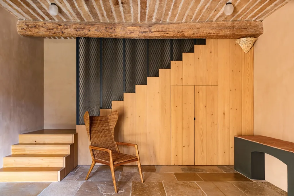 Wooden stairs above concealed storage beside a woven chair at Fabrègues, Pierre Yovanovitch