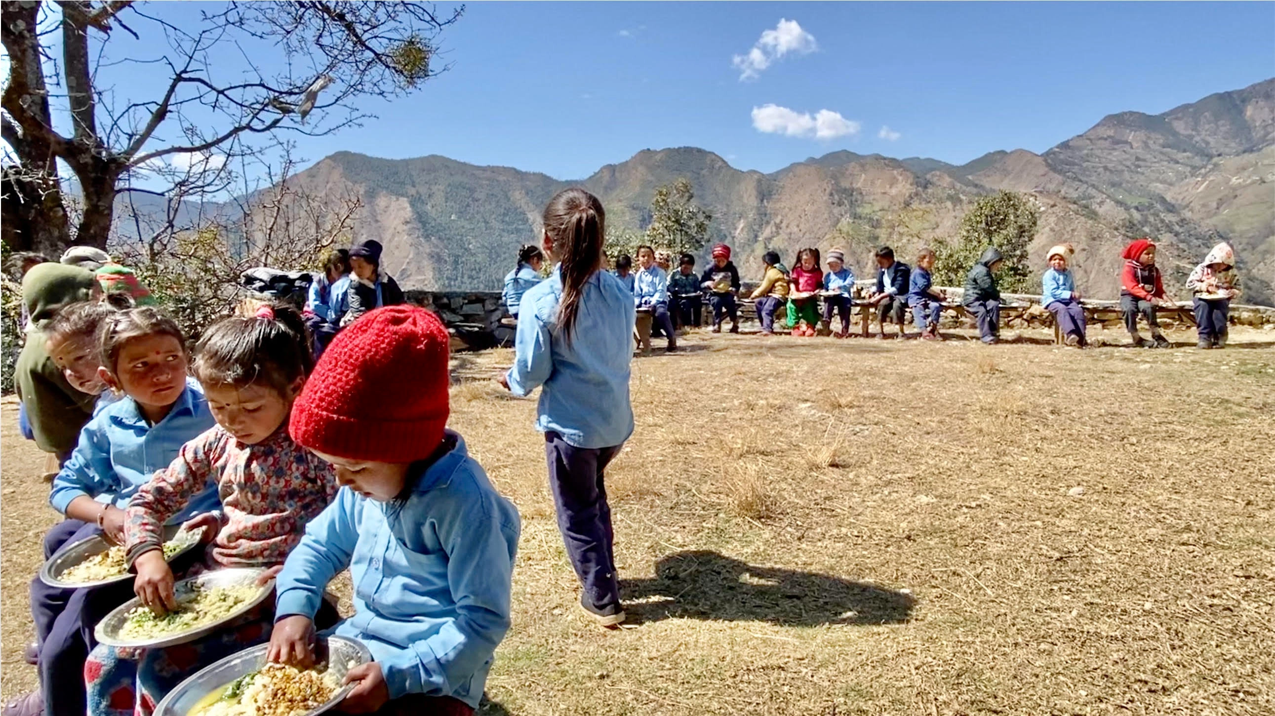 Kids sit on benches to eat their lunch of dal bhat outside at Shivbhawani Primary School, Deulekh, Bajhang