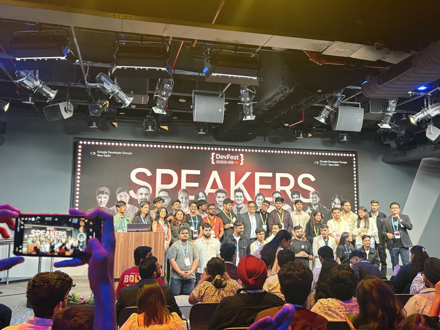 The DevFest speakers lined up on stage for a group photo under a large SPEAKERS banner.