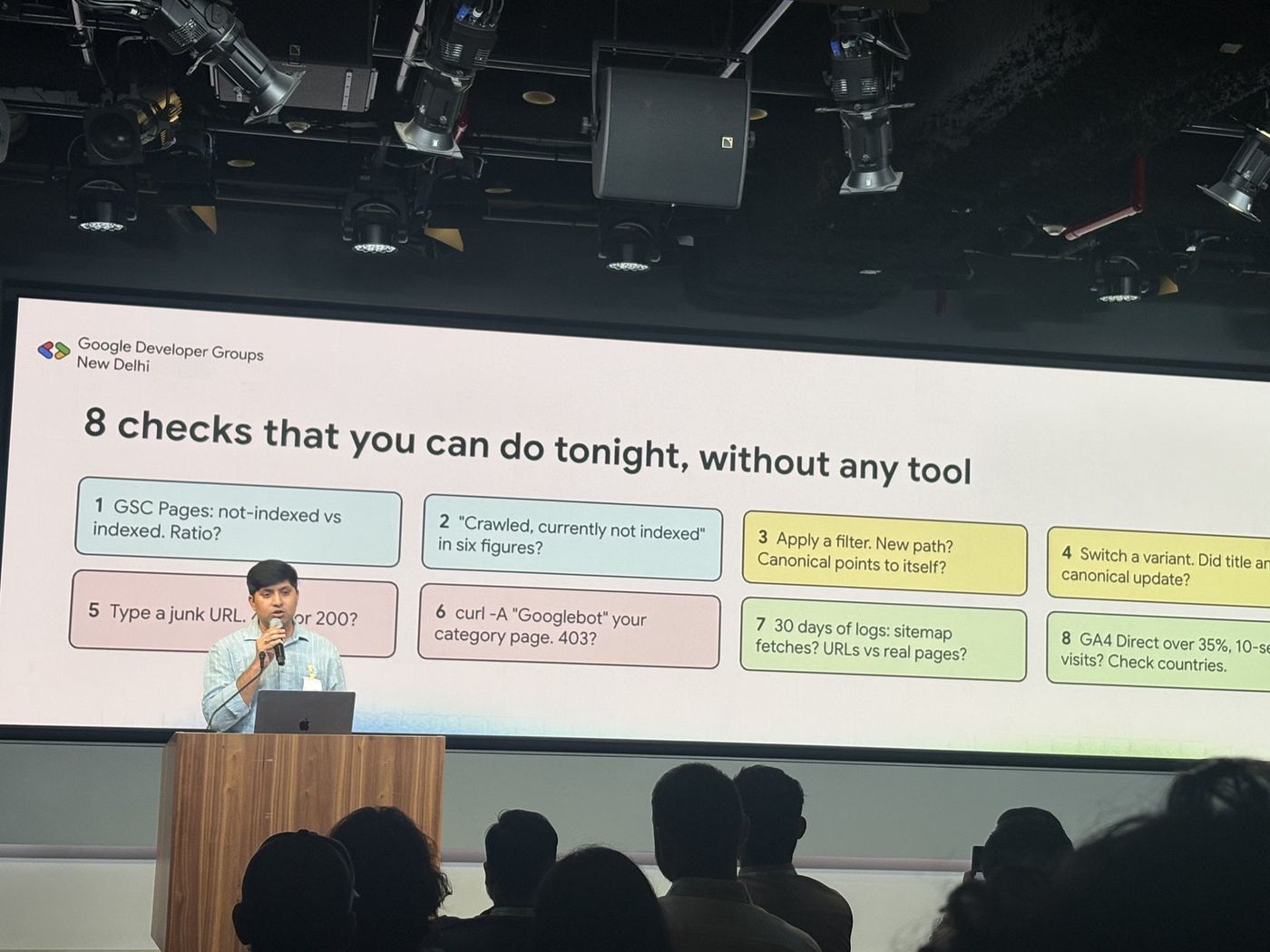 A speaker presenting a slide titled "8 checks that you can do tonight, without any tool" on URL structures, crawling and logs.