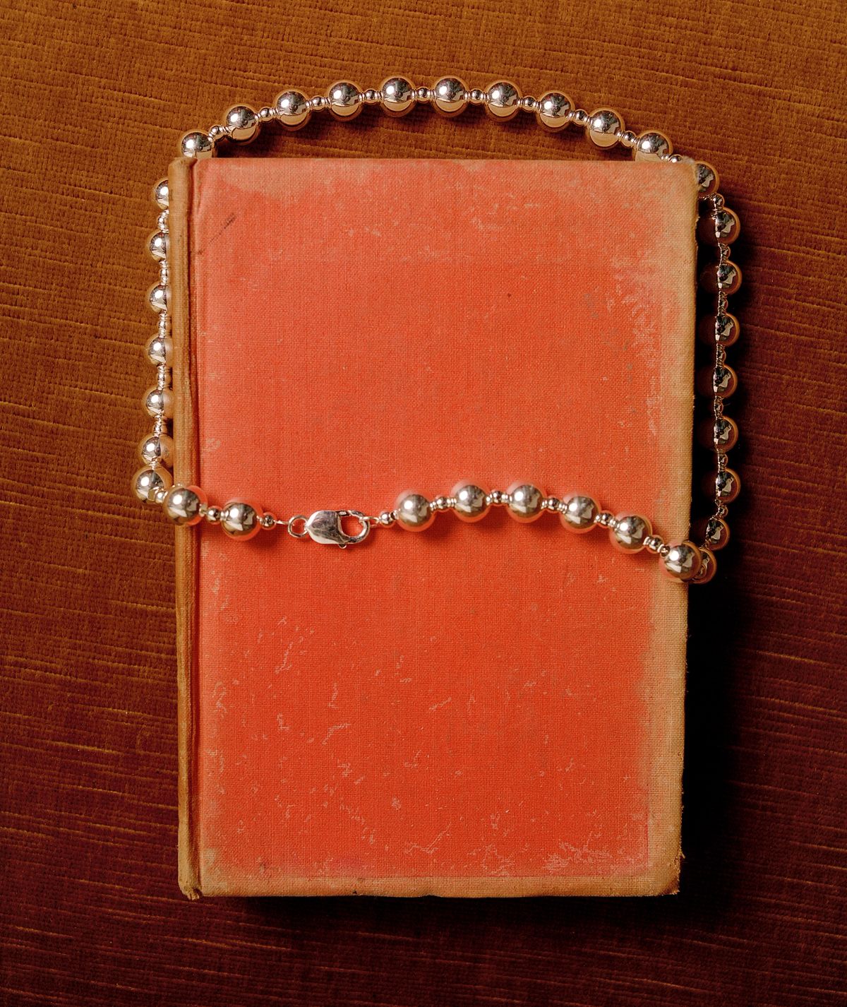 A silver necklace on top of faded red book on top of a wooden table