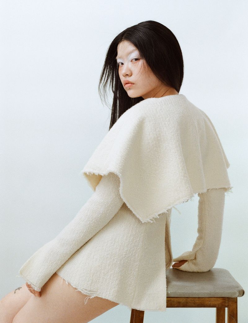 model wearing white sitting on stool on a white backdrop