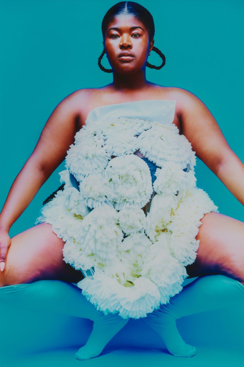 Model squatting on a blue backdrop with a white fully dress