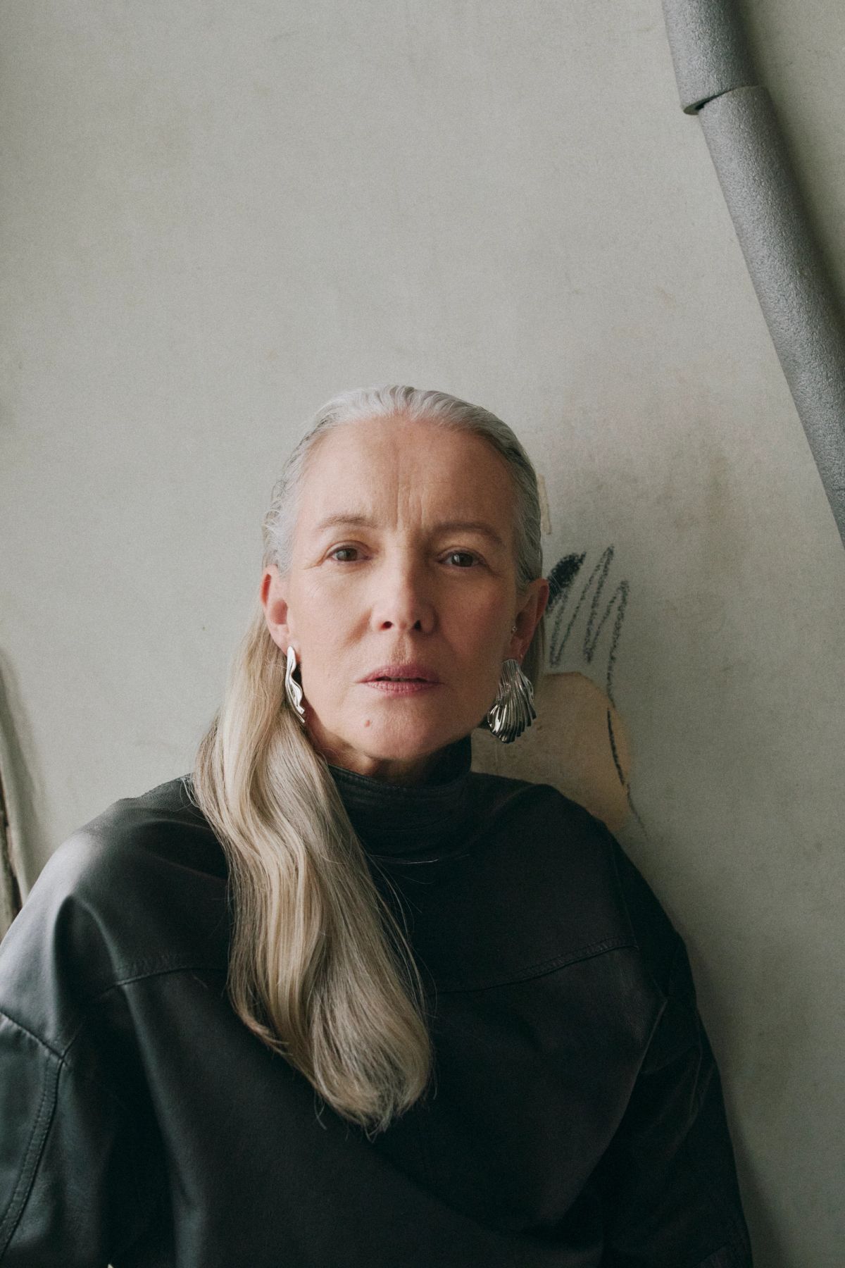 women with grey hair stares directly into the camera wearing a leather top and silver earrings