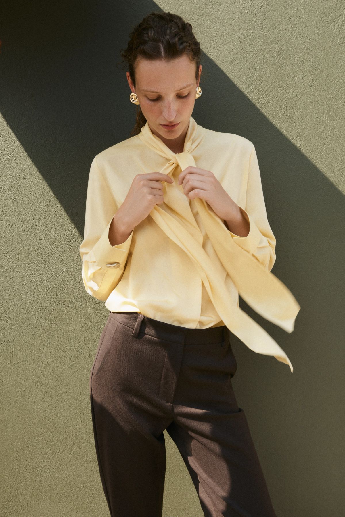Woman standing by green wall tying yellow blouse