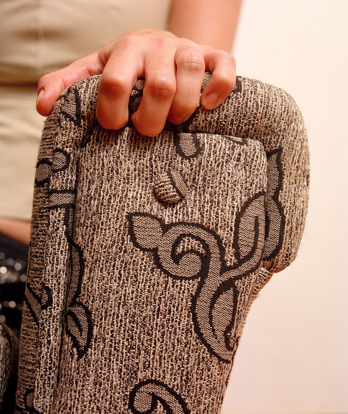 A hand grasping at the edge of a brown patterned sofa on a cream background