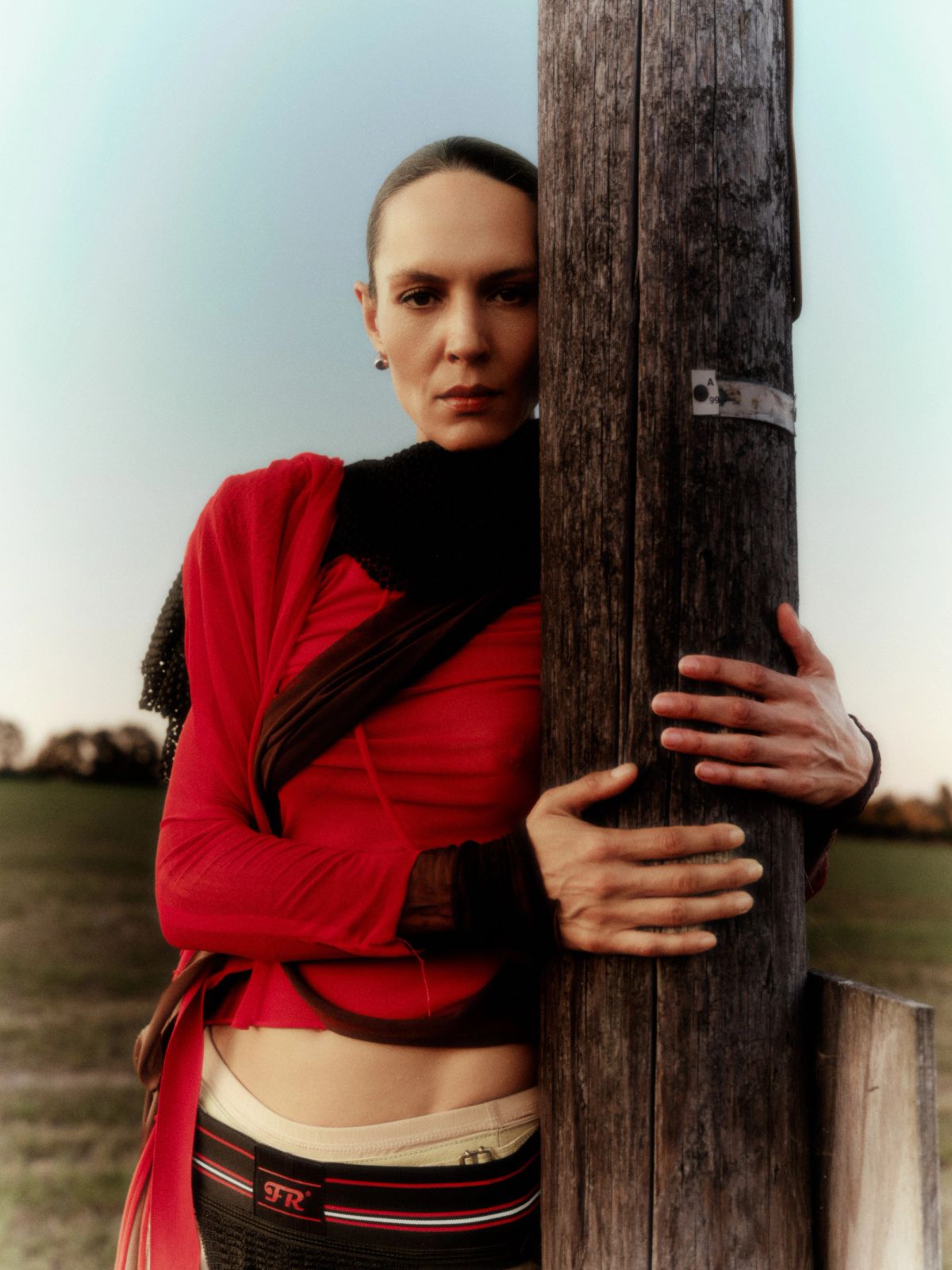 portrait of a model wearing red standing in a field holding on to a post