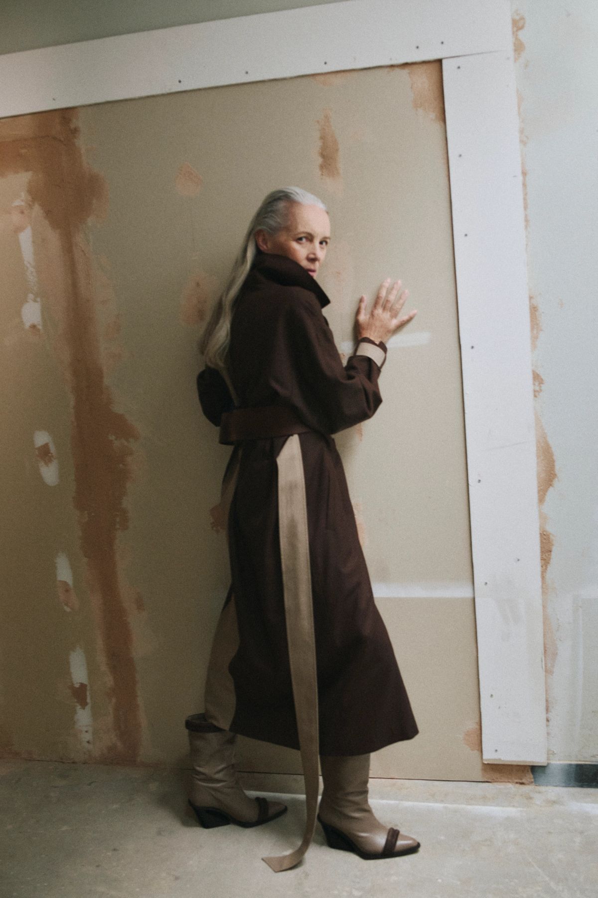 women leaning against a wall wearing a brown trench coat