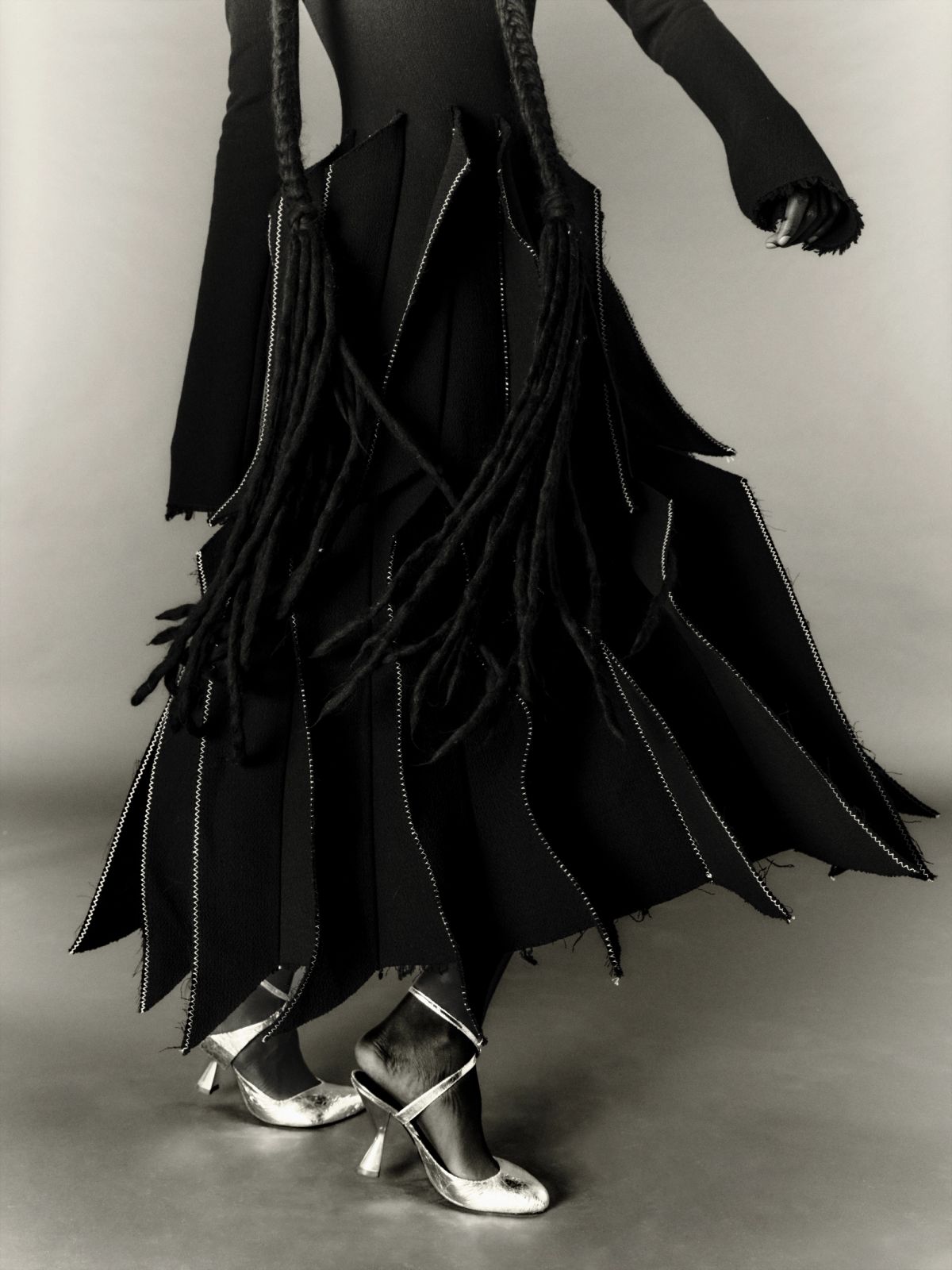 black and white image of model waist down wearing black dress and silver shoes