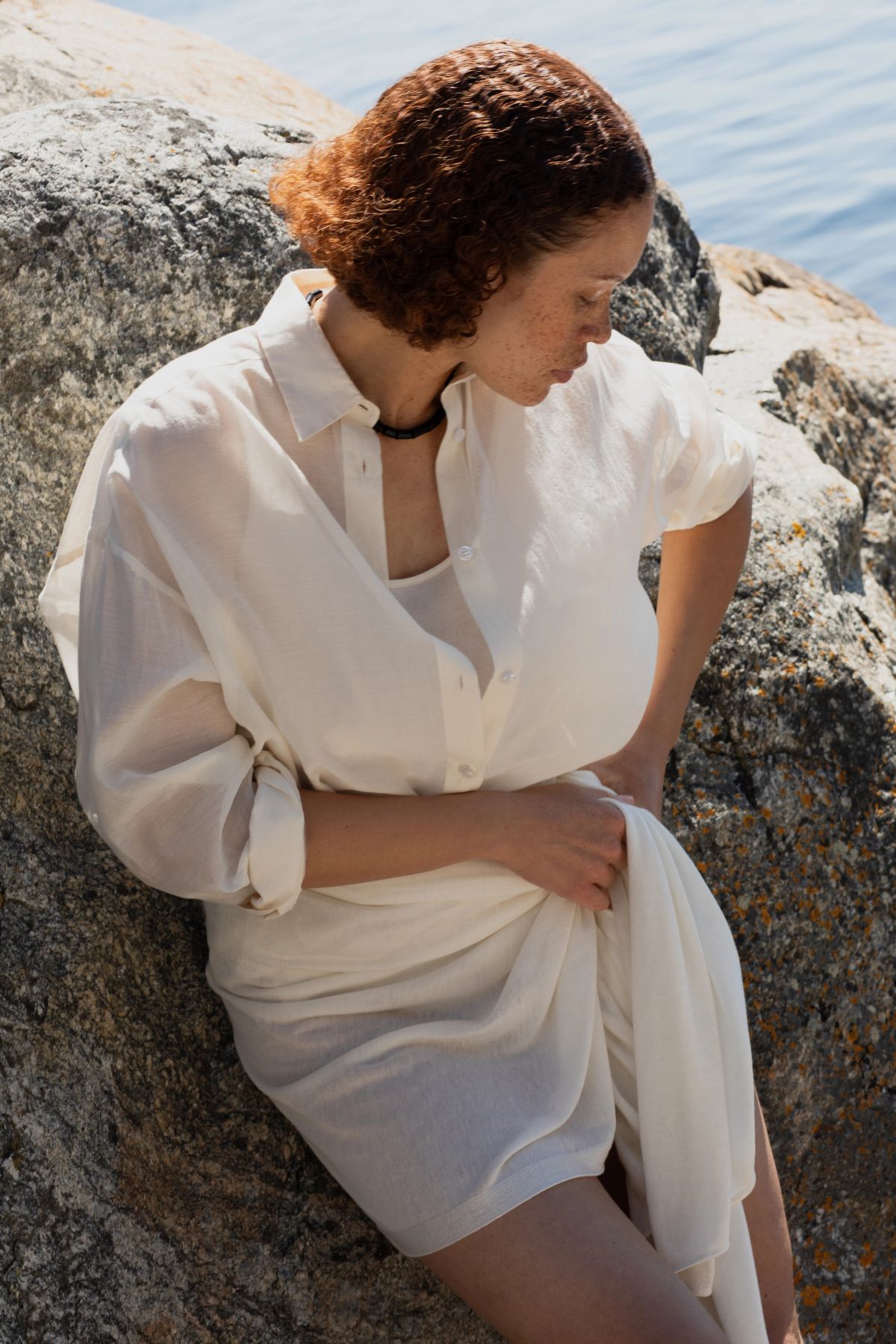 women ties her dress as she leans on a cliff