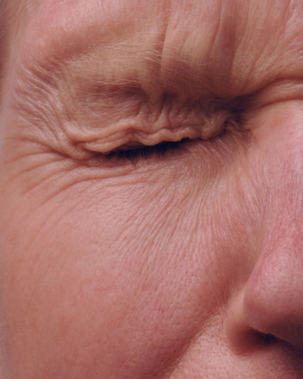 a close up of a womens eye, closed tightly showing the skin creasing