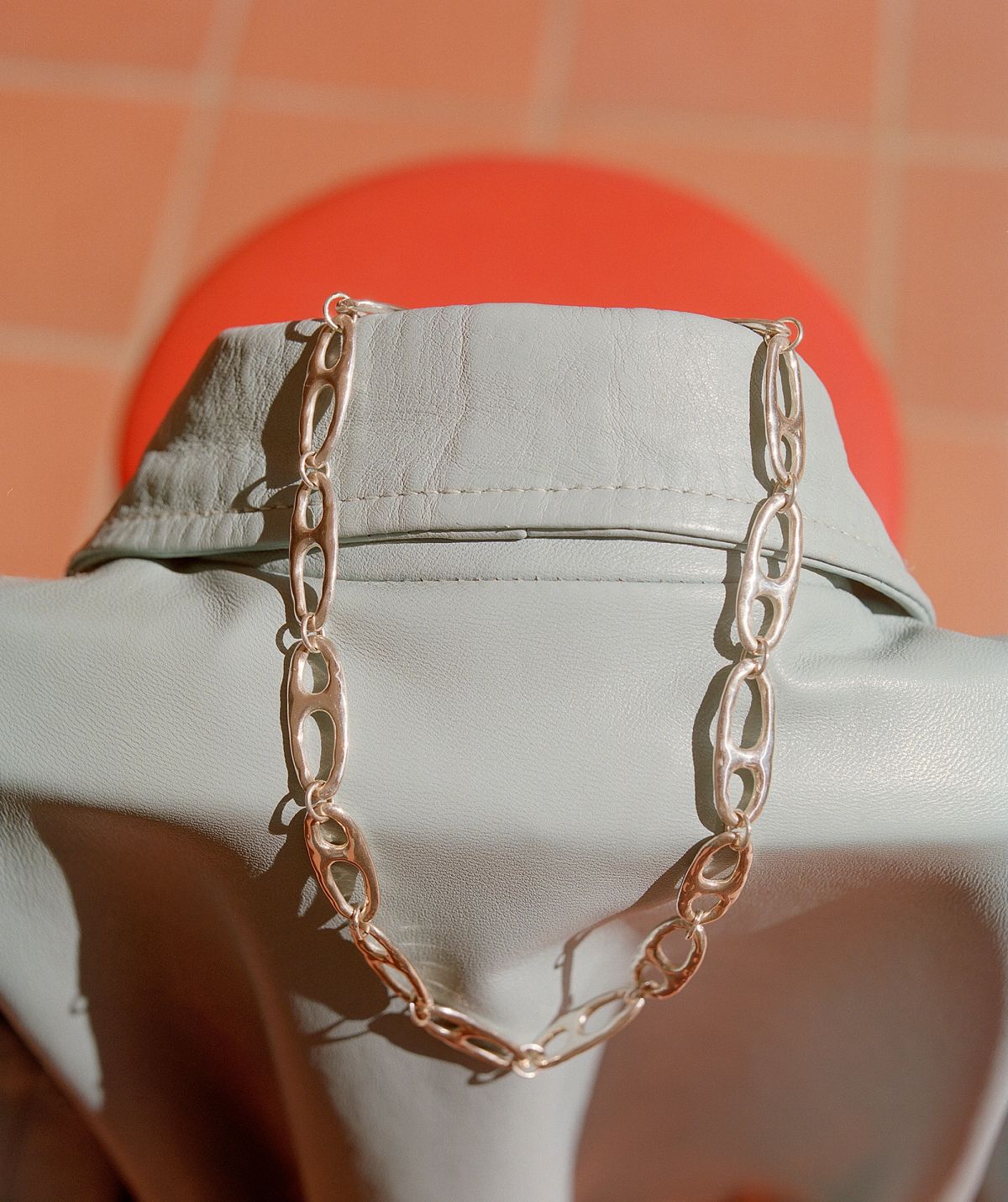 A silver necklace with large links draped over a white leather shirt, draped over a chair 