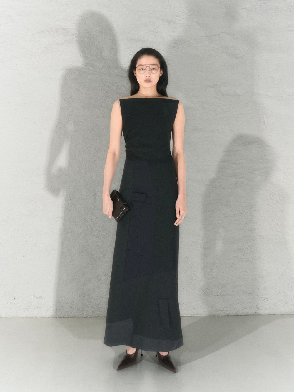 Women standing in a black column dress in a white studio holding black bag