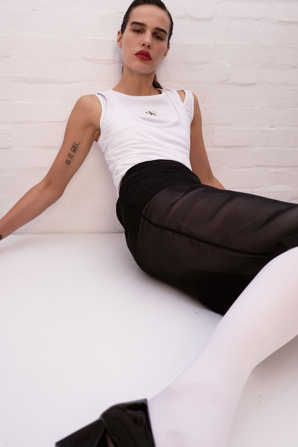 women sitting on a white table, wearing a vest and skirt with white tights