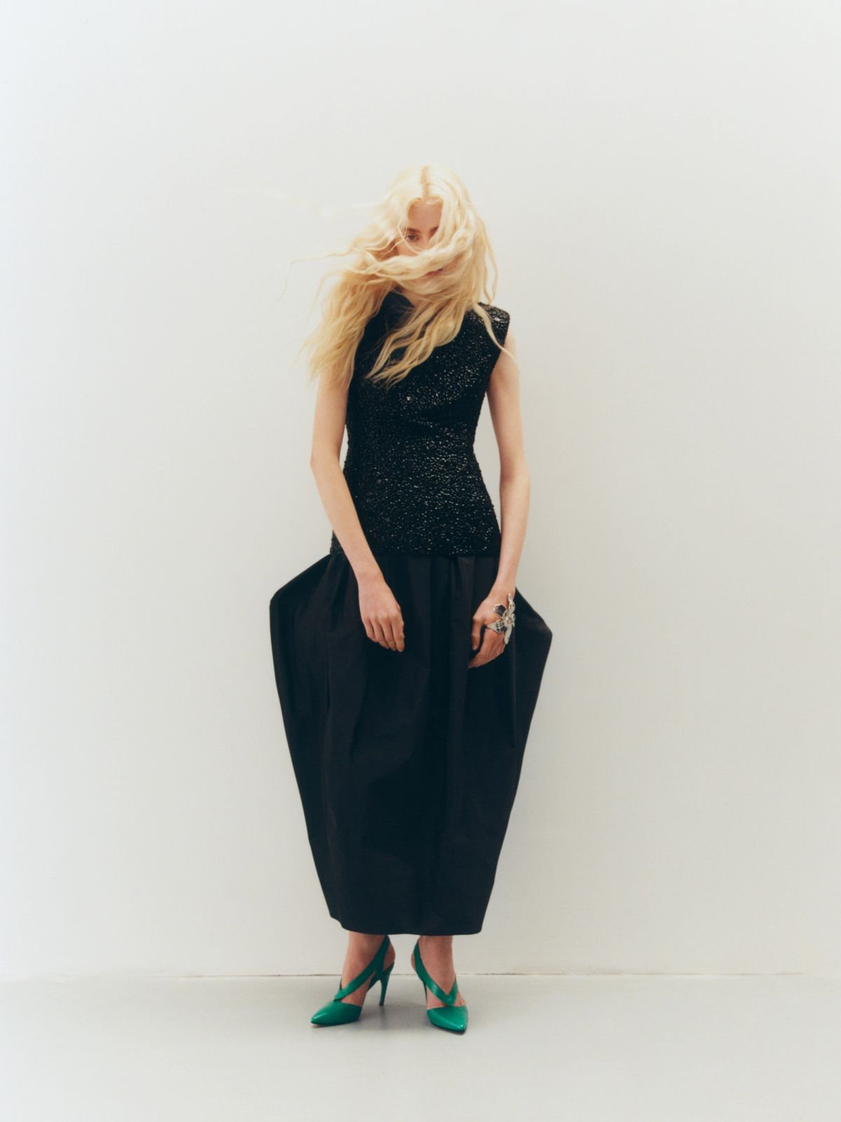 Women stadning in a white space wearing black sculptural dress and green shoes