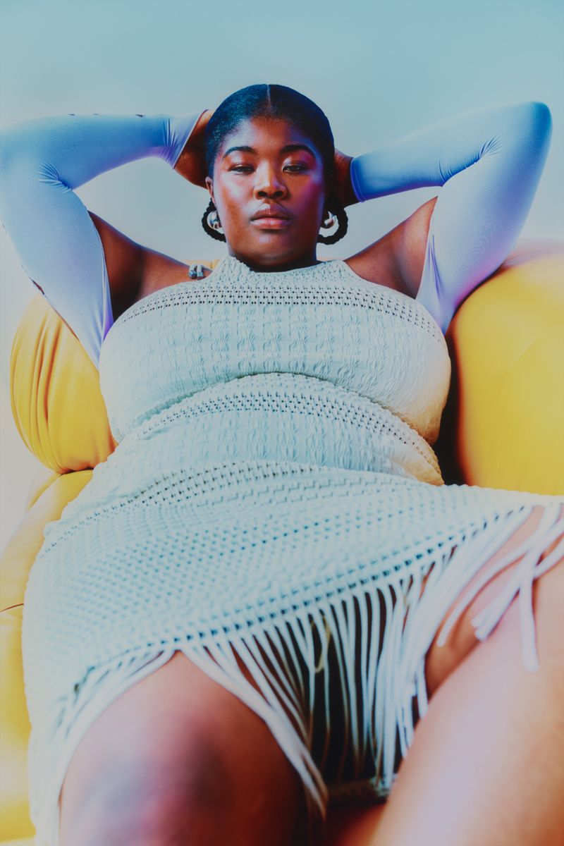 Model lying on yellow sofa looking to camera in a fringed dress