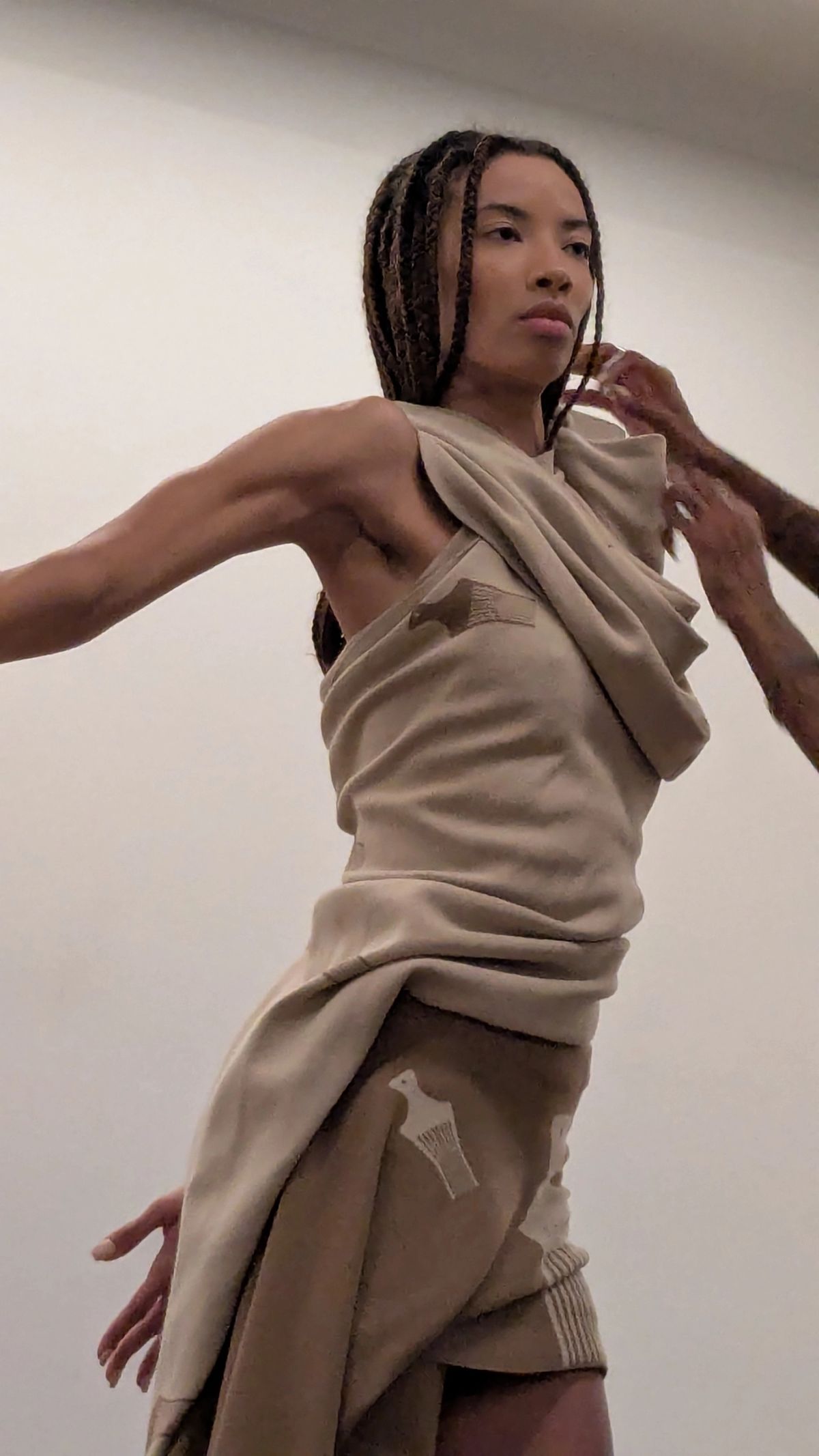 hands draping beige clothing on to a model while she moves