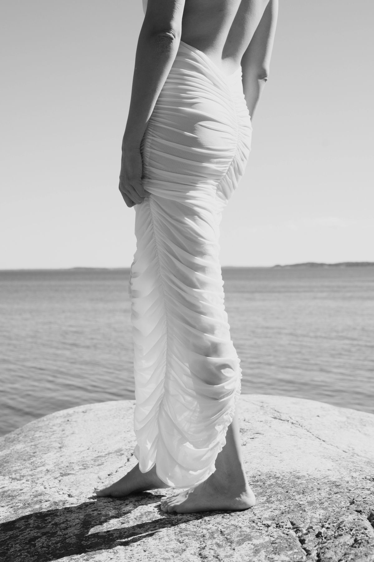 croped shot of woman in draped white dress standing on the cliffs by water