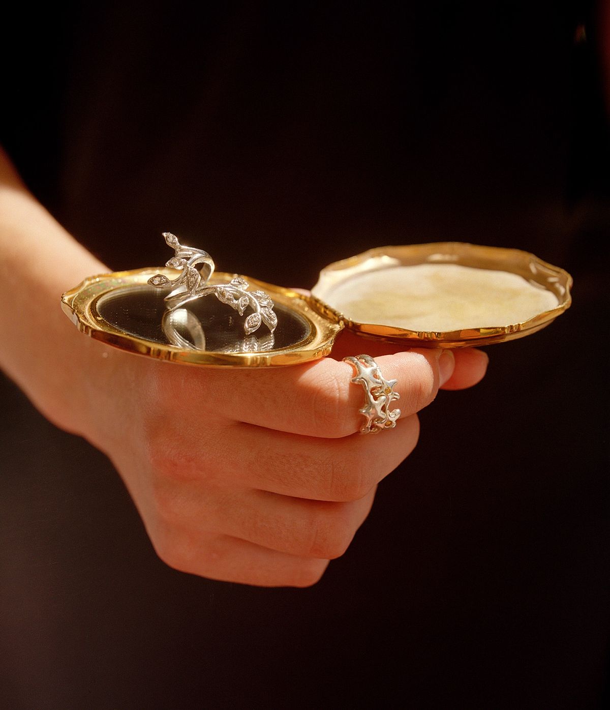 a ring, balancing on top of a vintage compact mirror being held by a women on a black background