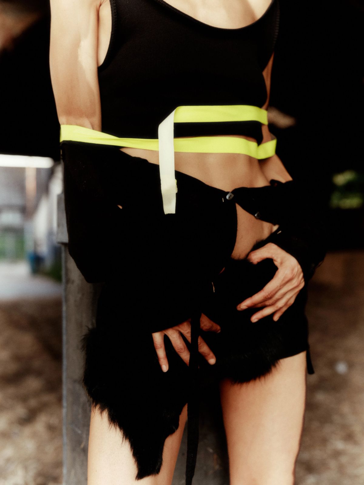 cropped shot of a models body wearing black with neon tape around the waist in a barn