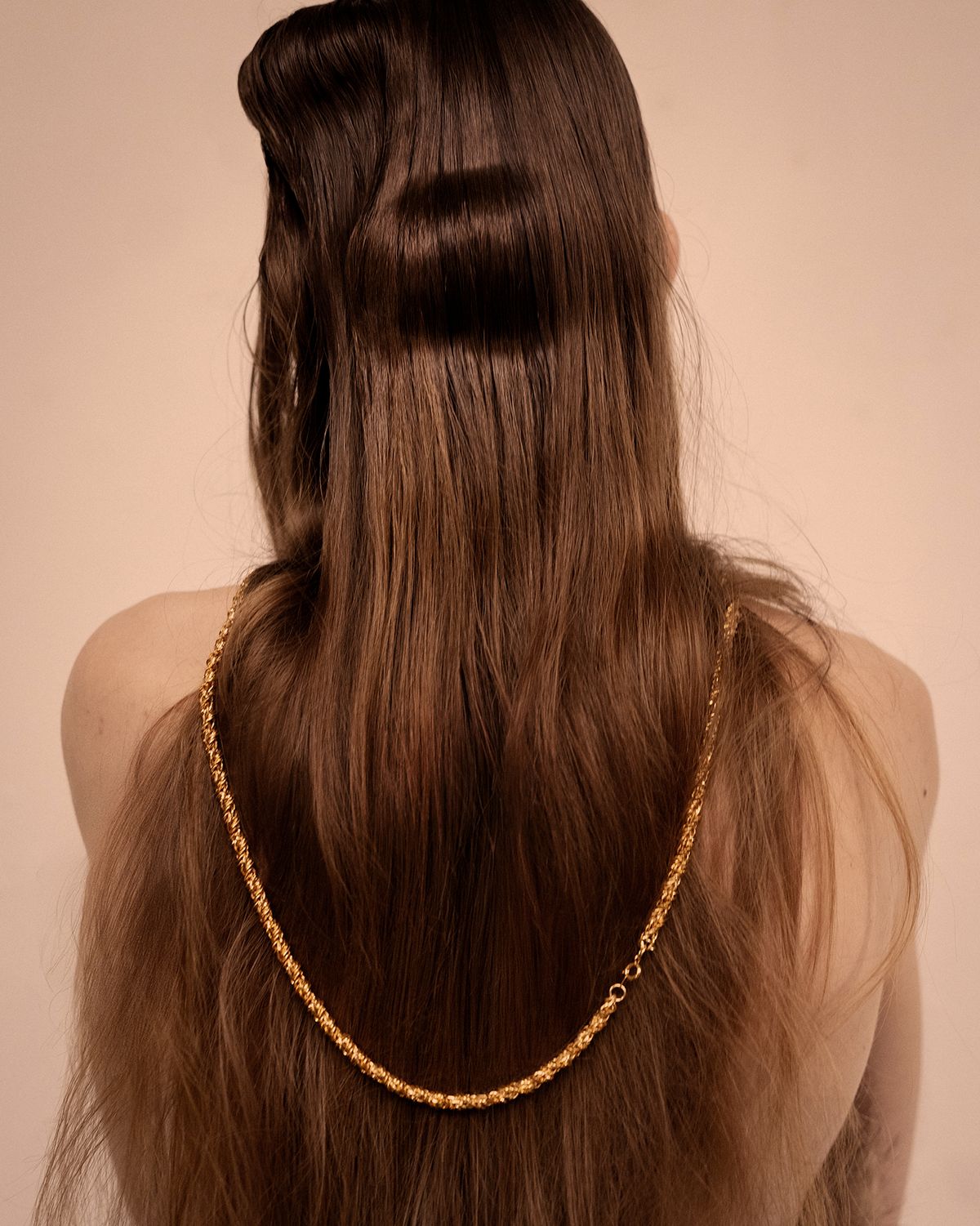 back of hair with a large kink and gold chain drapped across 