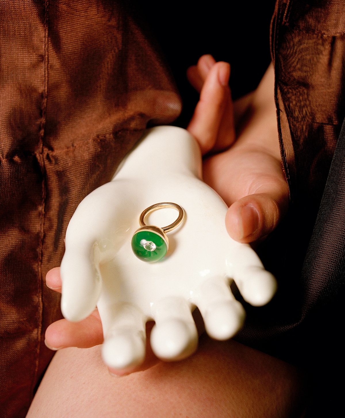 A hand holding a mannequins hand, holding a green ring