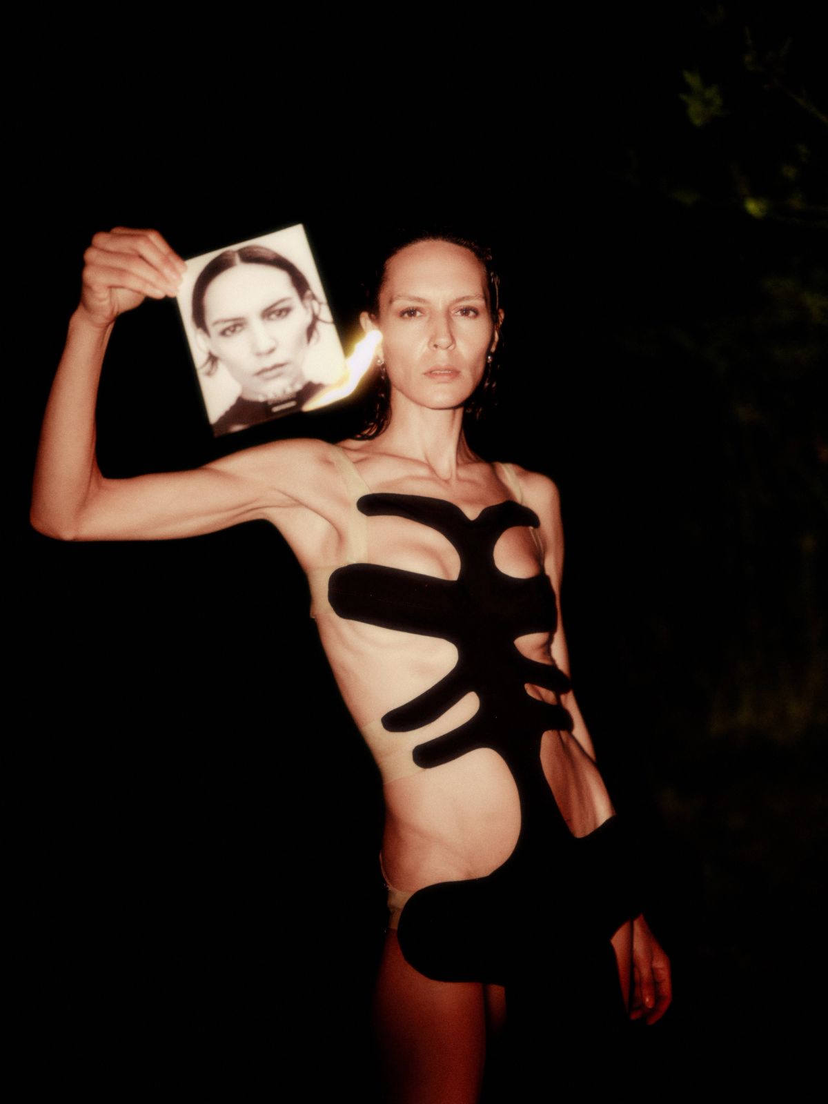 model in a black dress holding a burning photo of herself