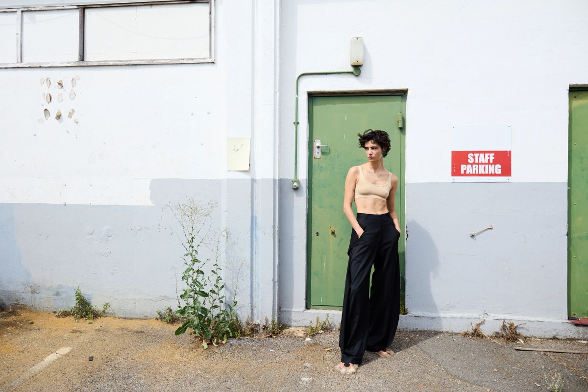 Woman standing by green door in black trousers and bra top