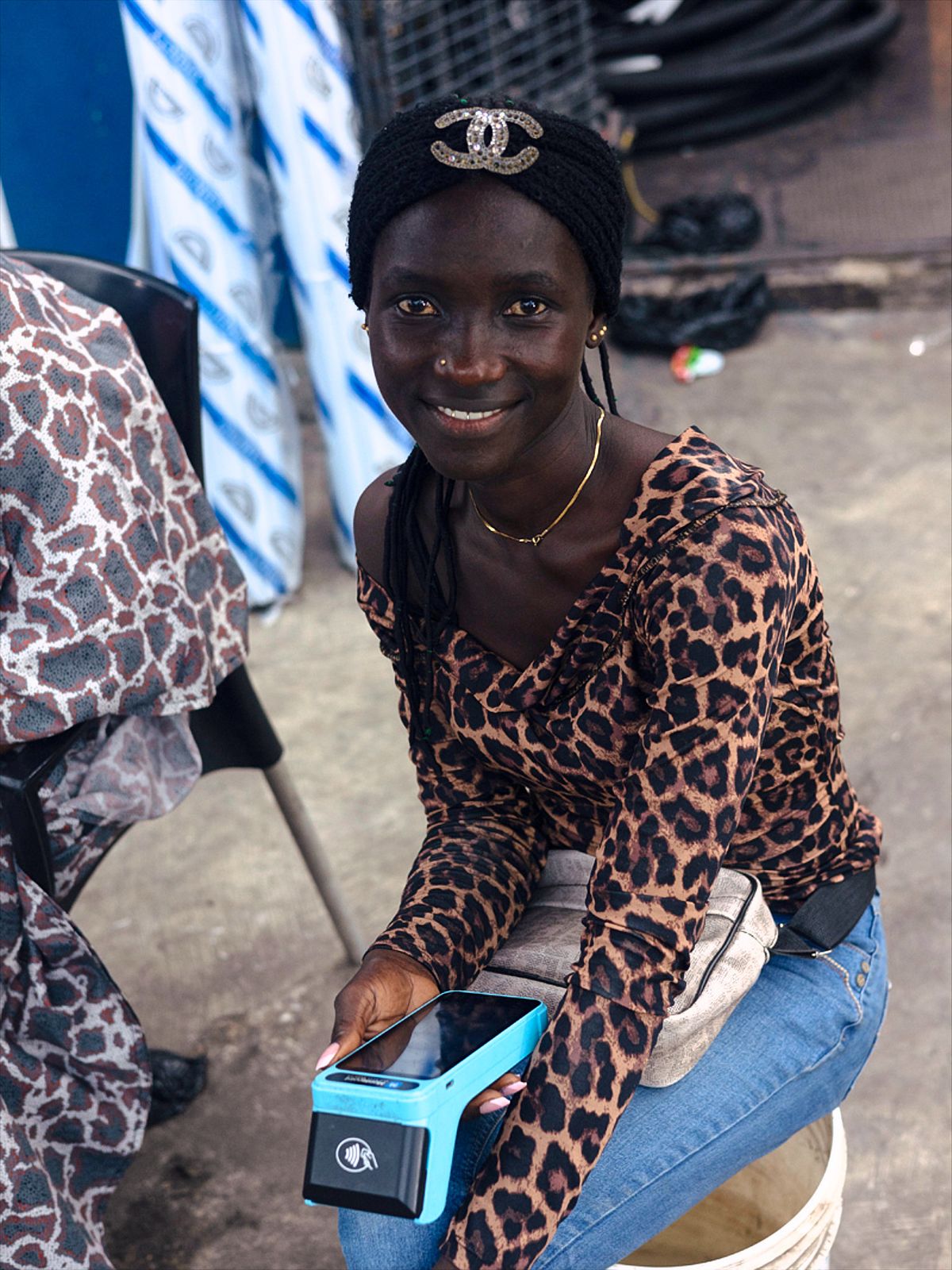 Young nigerian women with her POS machine sitting on a bucket wearing a chanel hat and leopard print