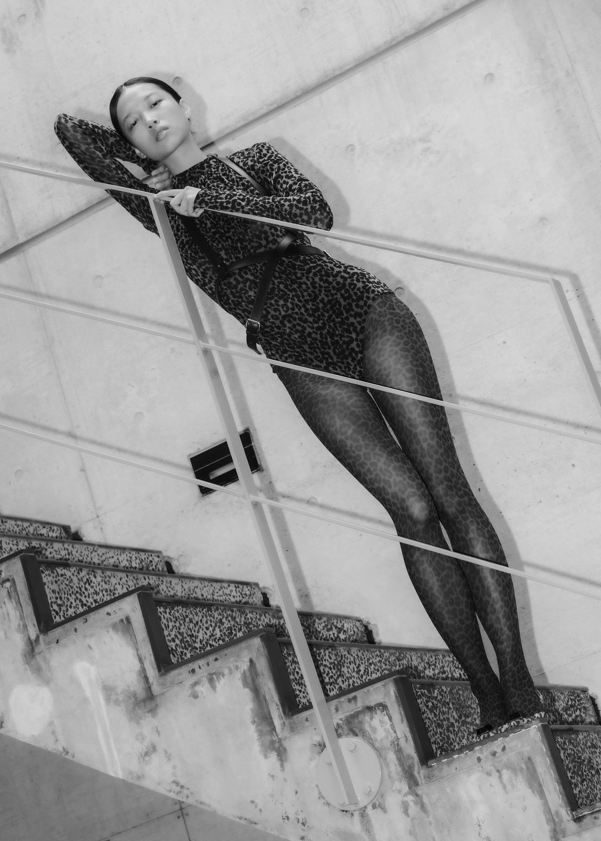 A model wearing a leopard print bodysuit and tights standing on a staircase