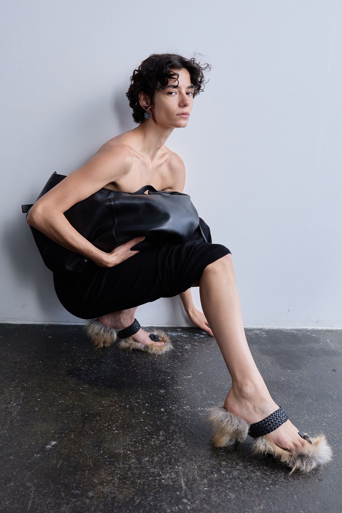 woman crouching on floor in black dress with bag and furry shoes