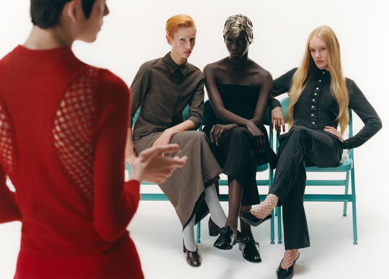 3 models sitting on blue chairs facing one model wearing red