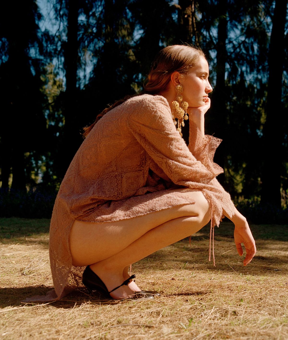 A women crouching on the grass wearing a beige dress and large earrings