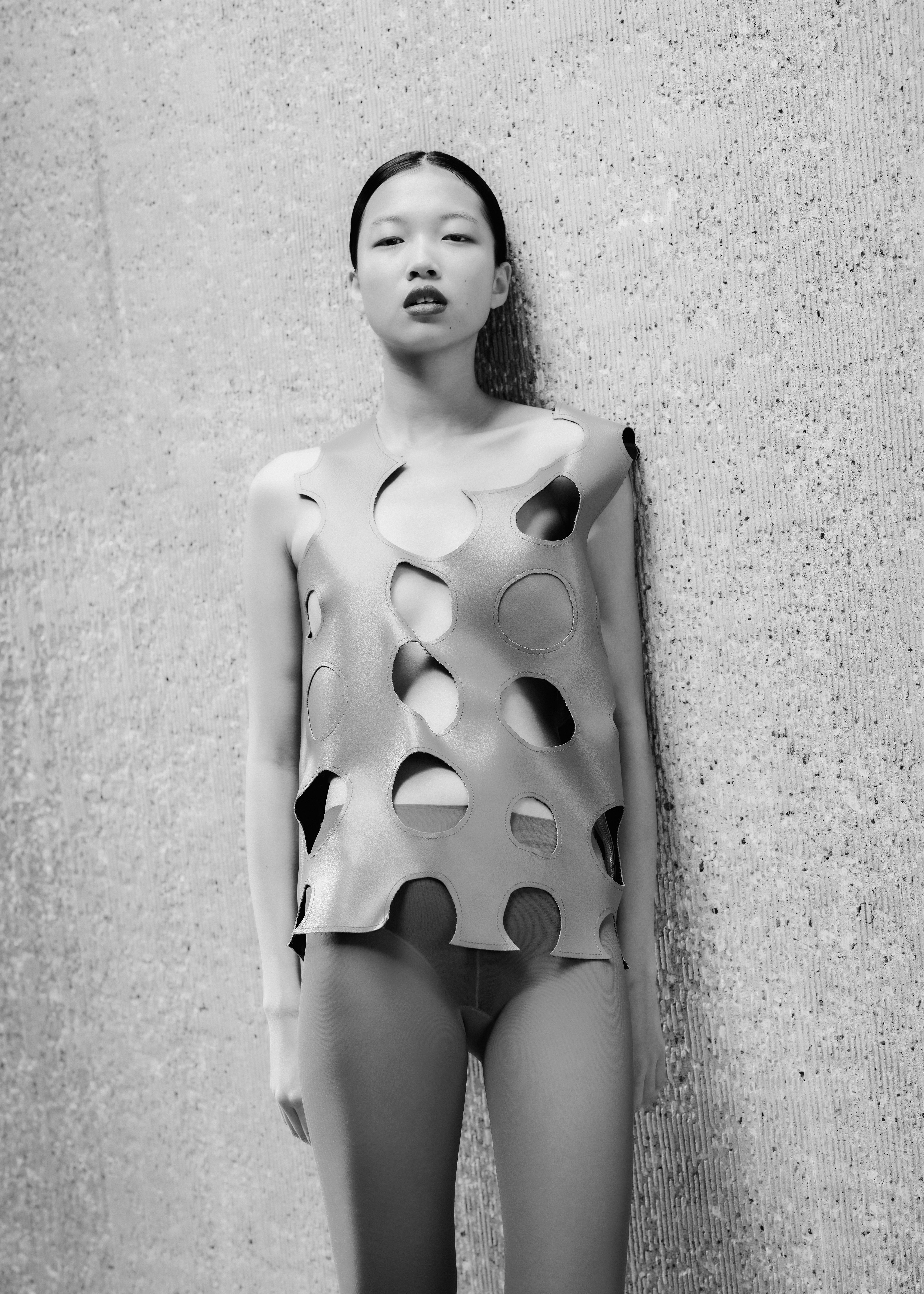A model standing on a concrete wall with holes in her top