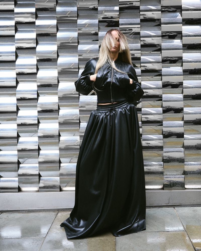 Women standing outside against a metallic wall in black leather top and skirt