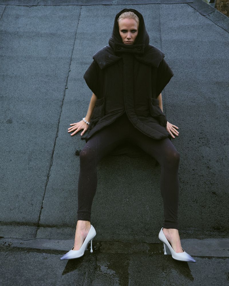 women in a black hoodie, tights and white shoes lying on wet gray paving slabs