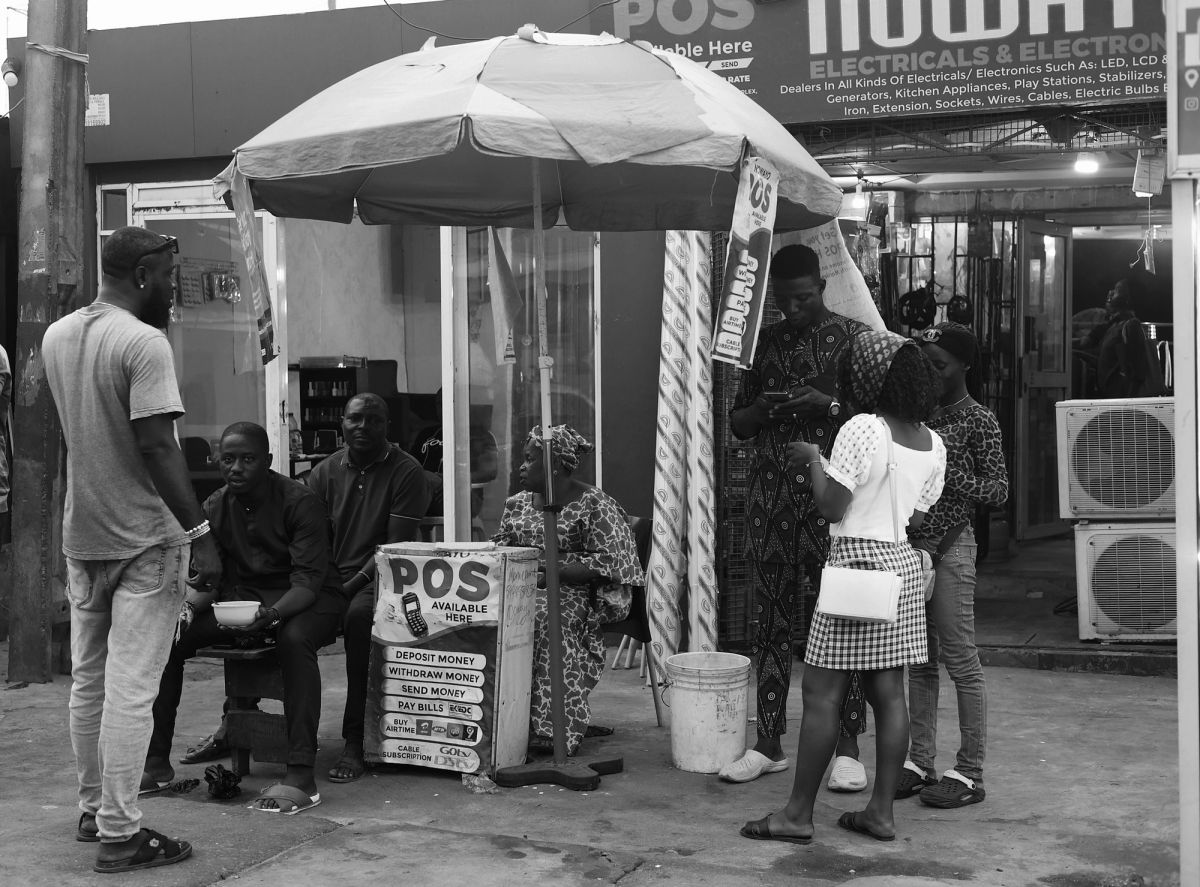 lagos Street scene of people sitting and standing around a stall with an umbrella