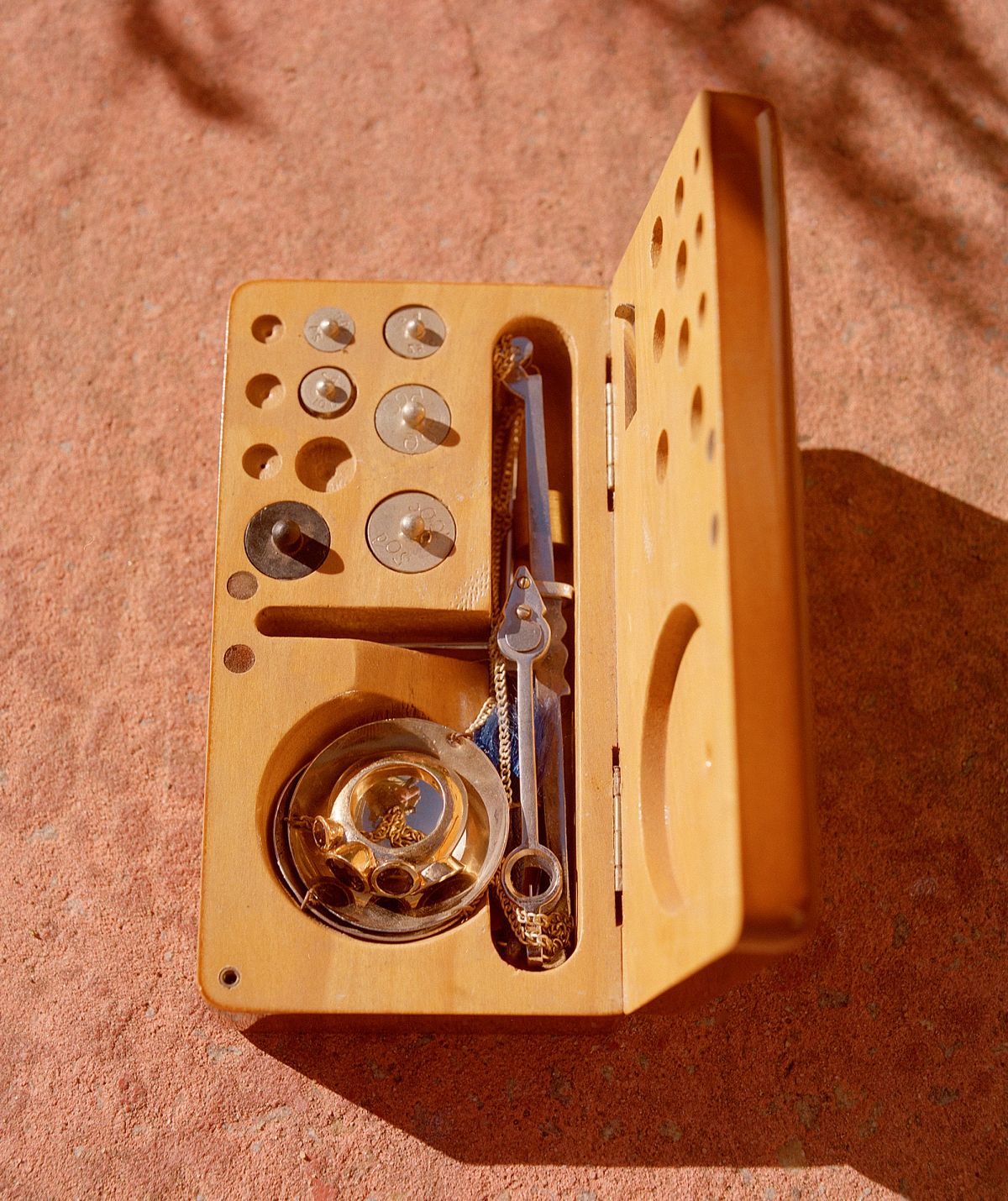 an open wooden tool box with jewellery inside shot on a terracotta floor