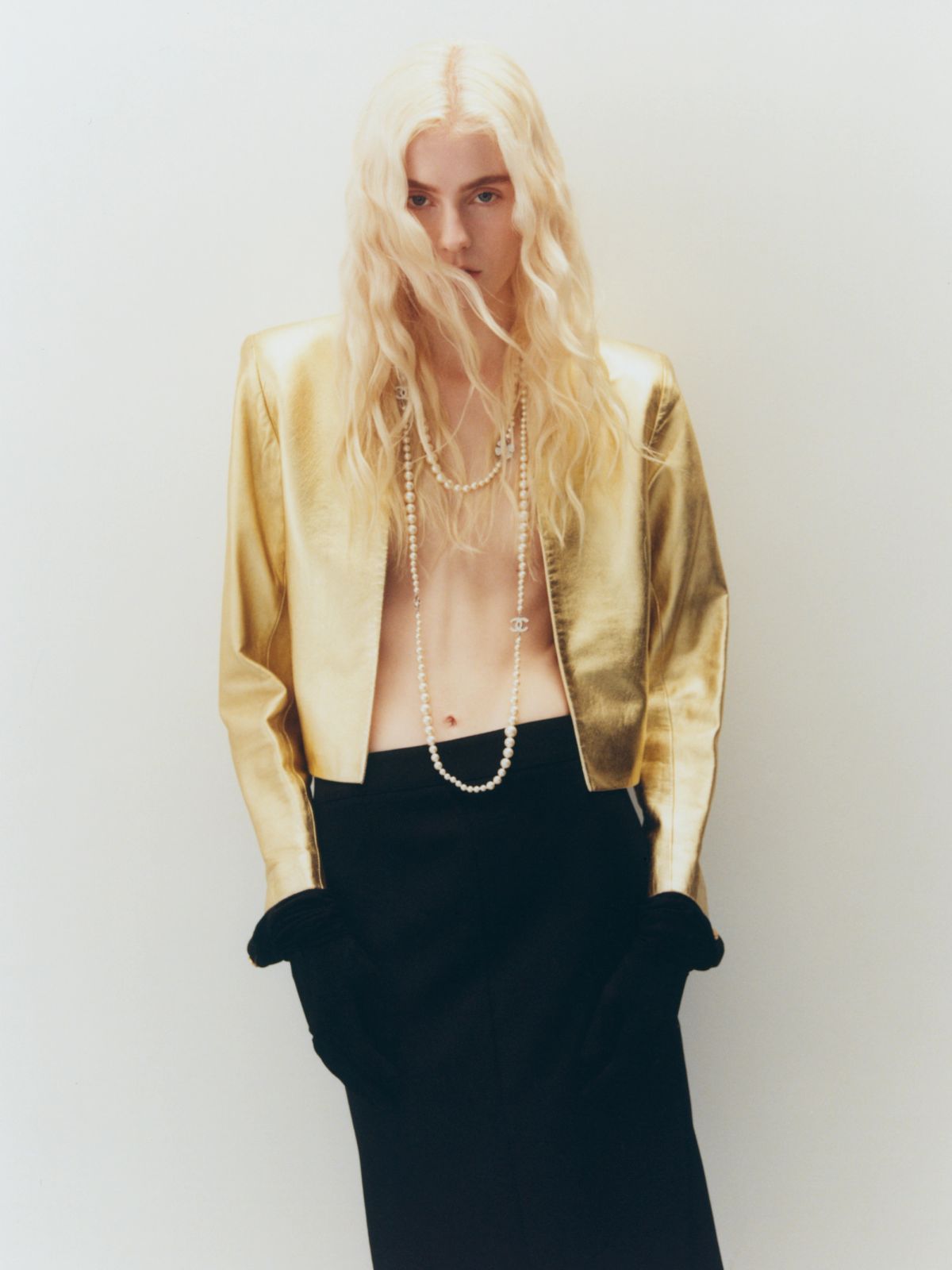 Women standing on a white wall wearing gold jacket and black skirt