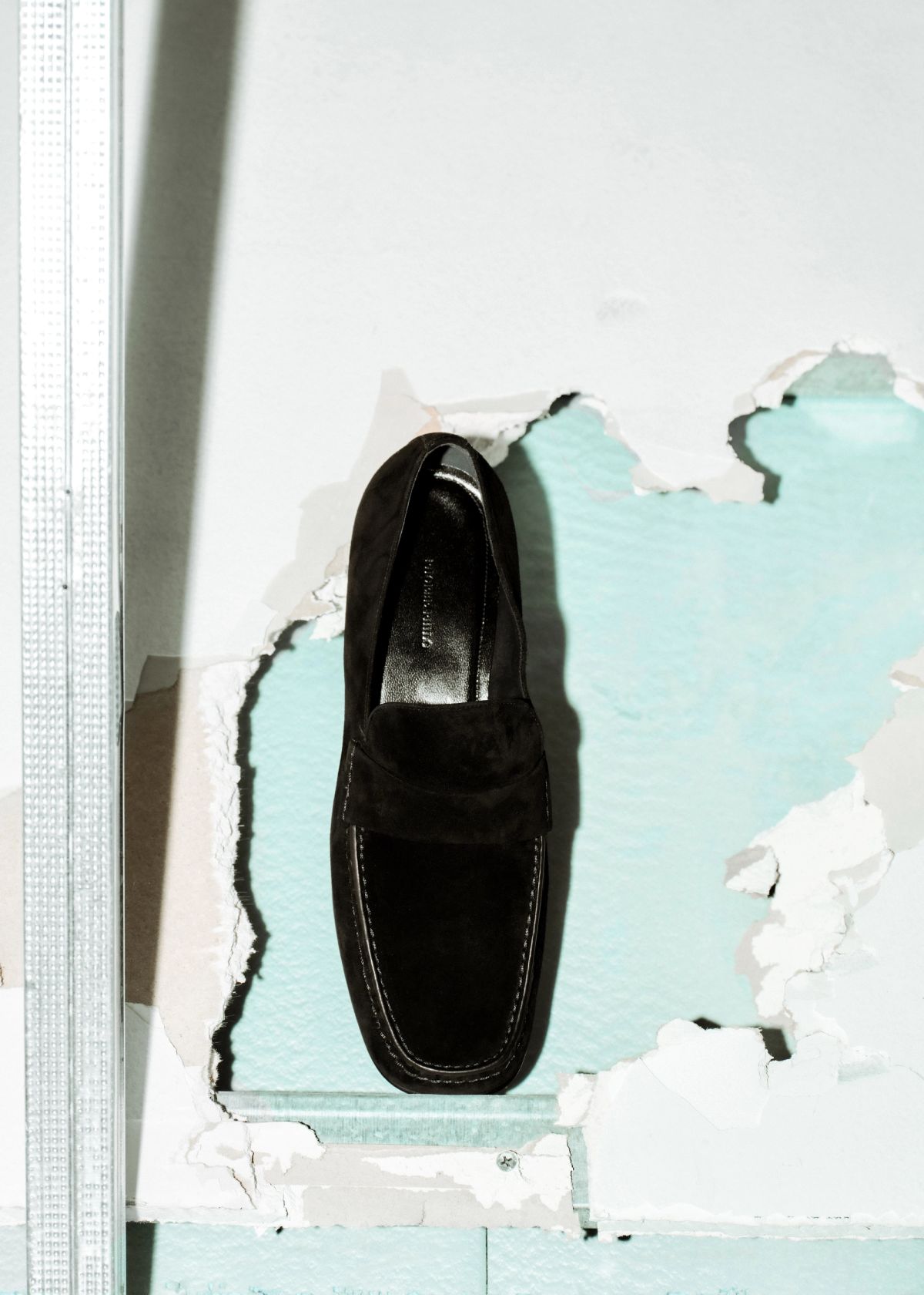 Loafer sitting on a broken plasterboard wall
