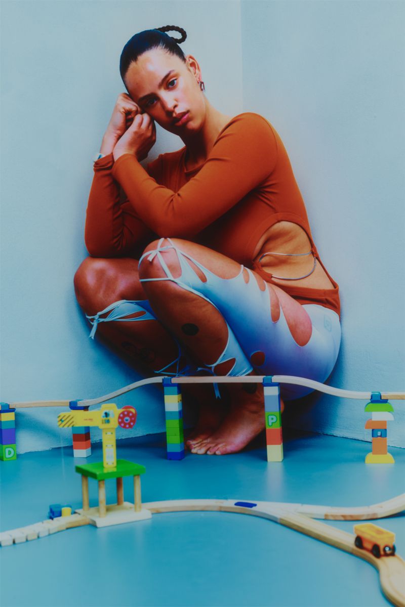 model in a corner wearing orange squatting behind a kids train track