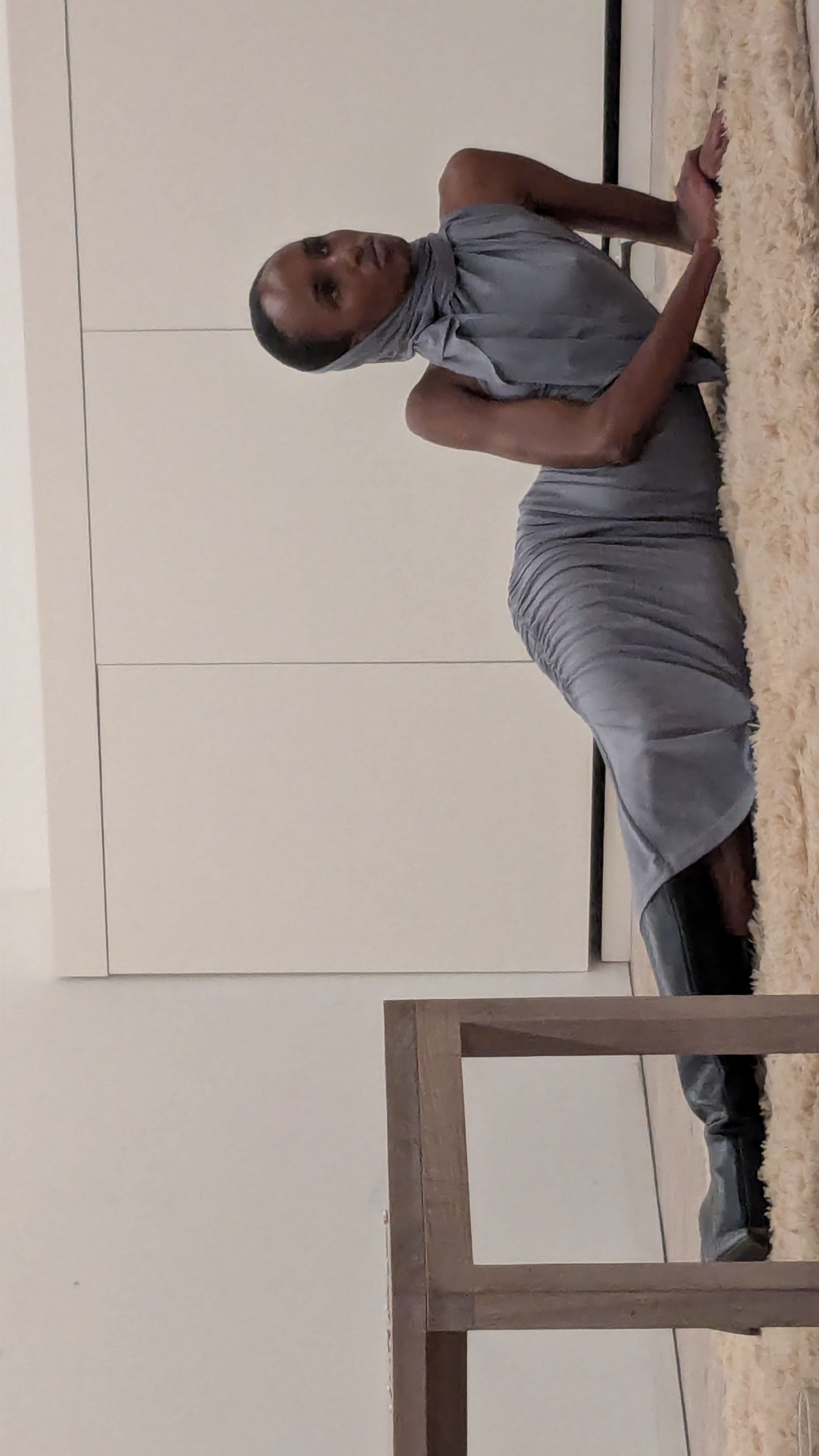 a model lying on a shag pile rug in a grey draped dress