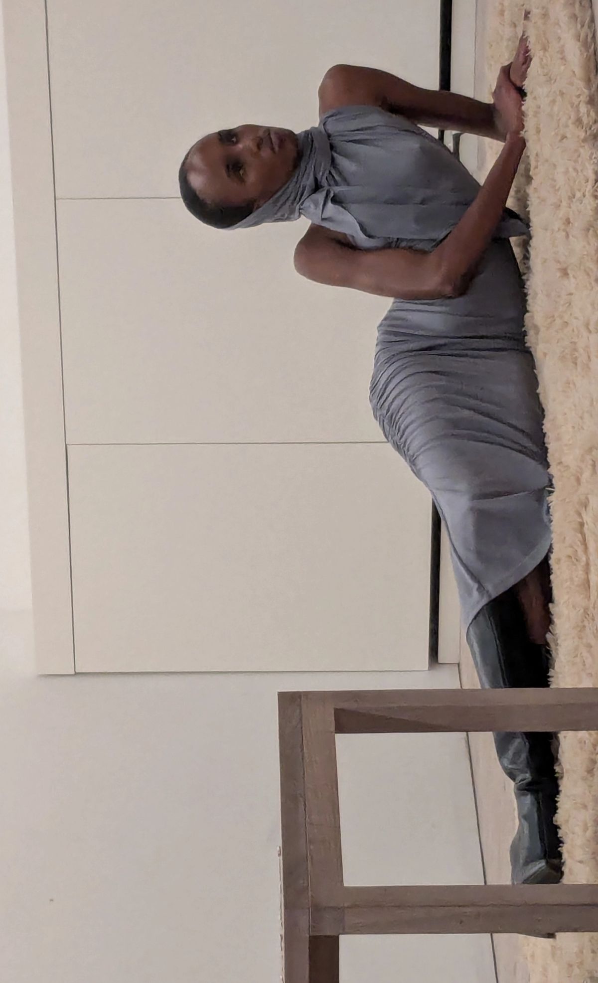 a model lying on a shag pile rug in a grey draped dress