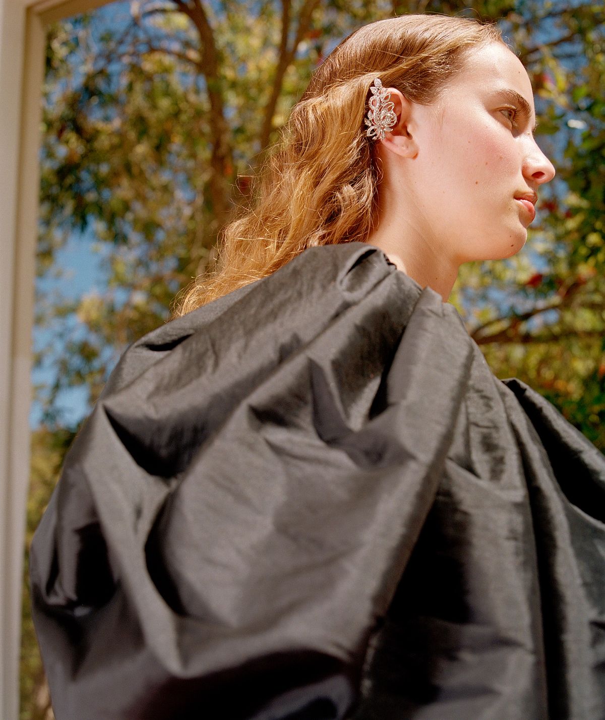 A model in a black dress and ear cuff standing outside
