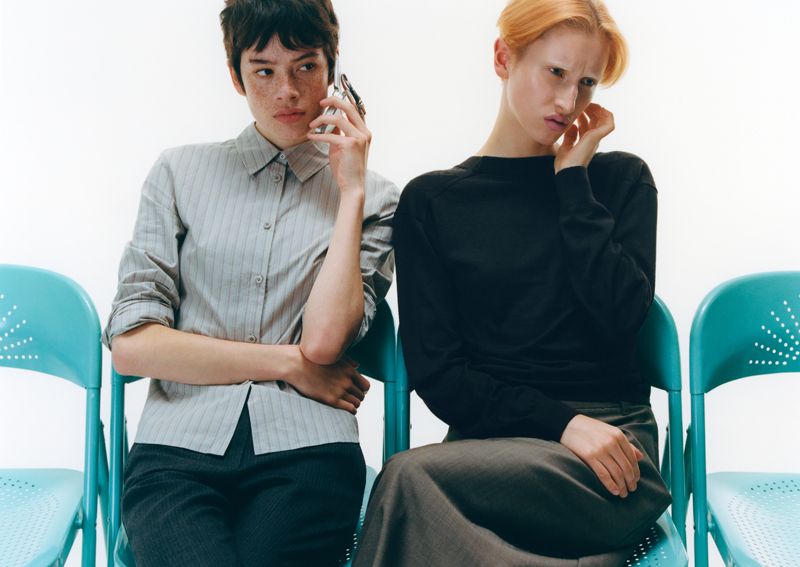 two models sitting on blue chairs, one on the phone, another touching her ear