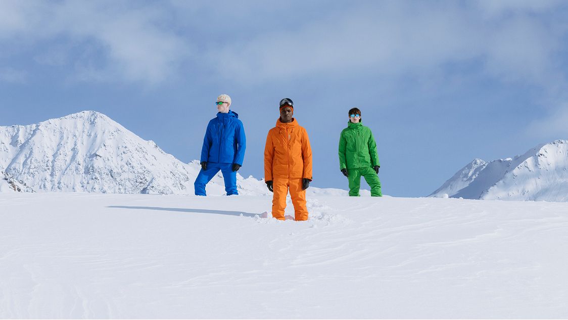 tre uomini sulla neve, giacca arancio, blu e verde